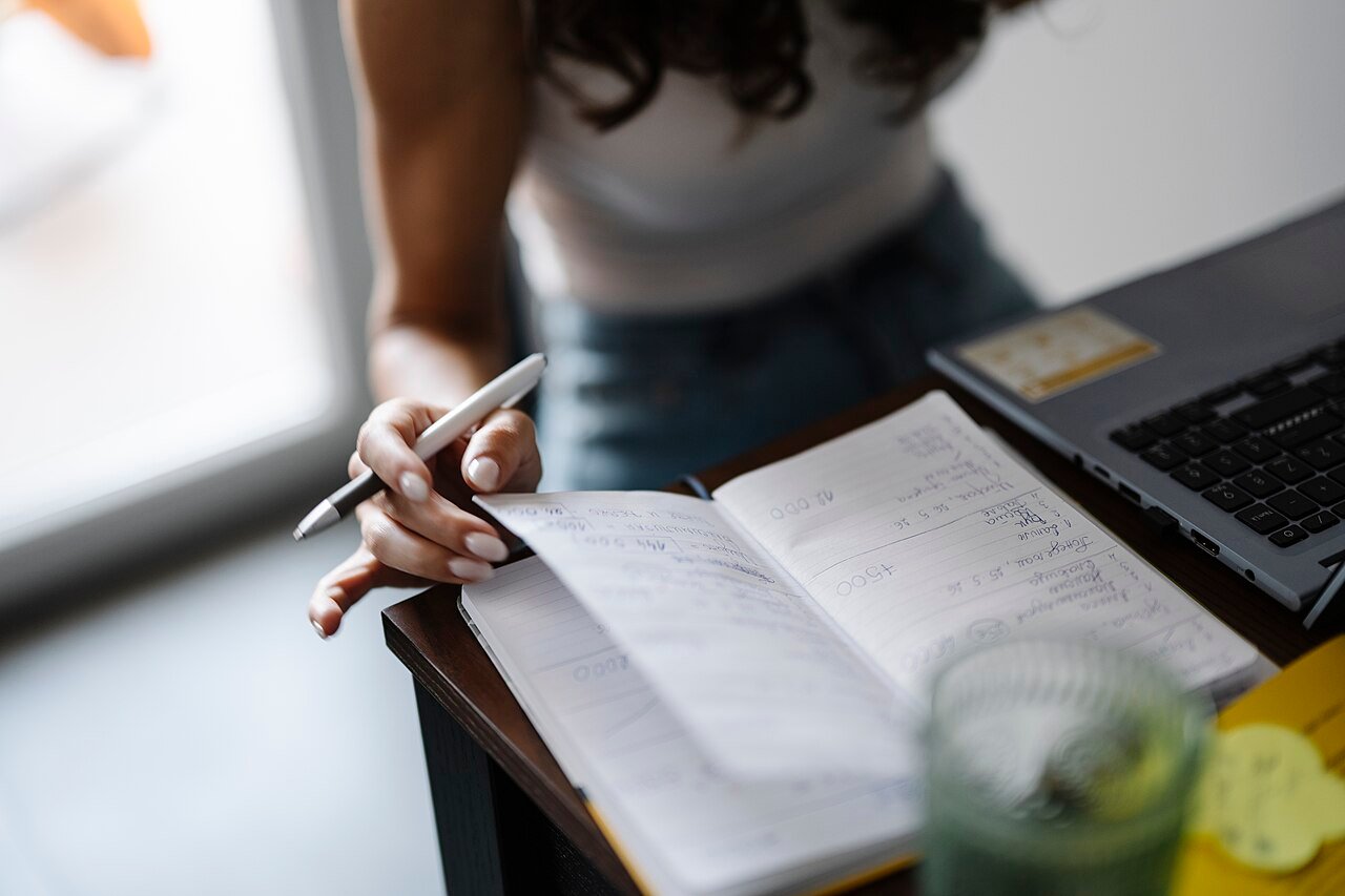 Persona anotando en un cuaderno junto a una laptop, como quien lleva un diario de síntomas